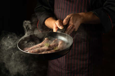Chef fry sausages on a hot pan with steam. Menu or recipe concept for hotel on dark background.の写真素材