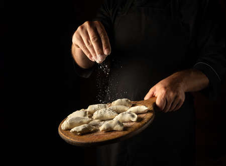 The chef throws flour on meat dumplings on a cutting board. Concept for a hotel menu on a black background with space for advertisingの写真素材