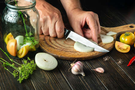Preparation of canned vegetable salad. Chef hands cut onion on a cutting board with a knife. Recipe...