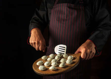 The chef prepares meat dumplings for lunch. Concept for a hotel menu on a black background with space for advertising.の写真素材