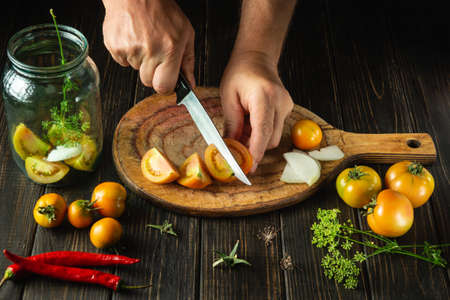 Preservation of vegetables in a jar. The chef cuts tomatoes on a cutting board. Peasant food.の写真素材