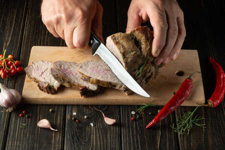 Slicing juicy beef steak with a knife in the hands of a chef close-up. The concept of cooking. Dark background for advertising or recipe.の写真素材