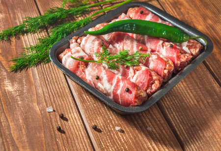 Raw meat Lula kebab wrapped in bacon in a plate on a vintage table with spices and pepper. Free space for advertising.の写真素材