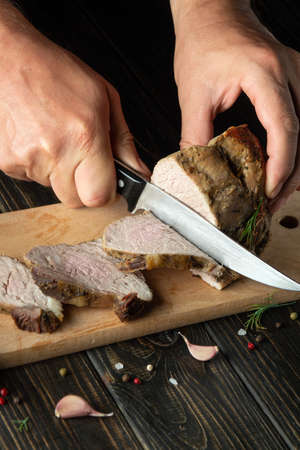 Cutting a juicy beef steak with a knife in the hands of a chef close-up. The concept of cooking. Dark background for advertising or recipeの写真素材