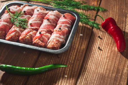 Raw meat Lula kebab wrapped in bacon in a plate on a vintage table with spices and pepper. Free space for advertising.の写真素材