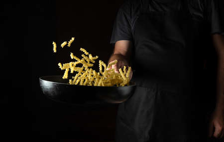 Professional chef prepares noodles in a hot frying pan with steam on a dark background. The concept of restaurant and hotel service.の写真素材