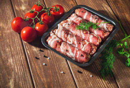 Raw lula kebab wrapped in bacon in a plate on a vintage table with tomato and dill.の写真素材