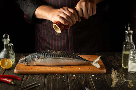 The fish chef adds pepper to fresh mackerel before preparing a delicious meal in the hotel kitchen.の写真素材