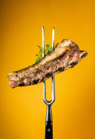 Baked beef ribs with spices and parsley on a fork after grilling or barbecue. Hotel or restaurant menu concept on yellow backgroundの写真素材