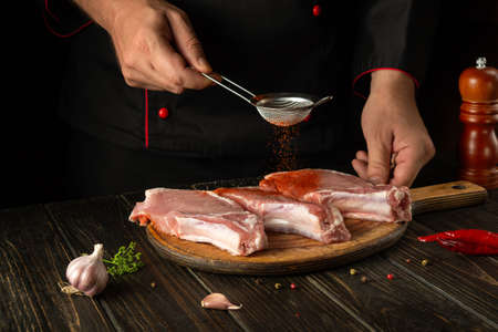 The cook adds paprika to raw meat ribs before grilling. Work environment on the kitchen table with spices and condiments.の写真素材