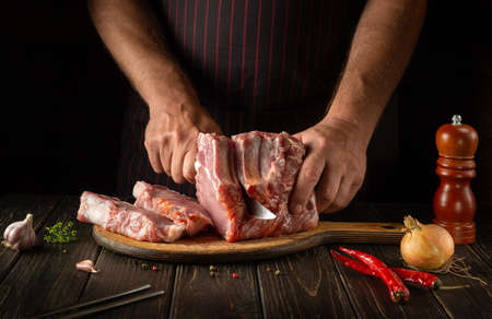 The chef or butcher cuts raw ribs on a cutting board before grilling. Meat dish idea for a hotel or restaurantの写真素材
