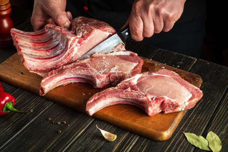 Experienced chef cuts raw meat. Butcher cutting pork ribs. Meat with bone on a wooden cutting boardの写真素材