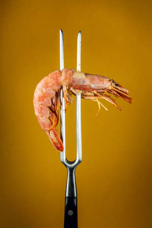 Boiled tiger shrimp or caridea on a fork. The idea of delicious food for a hotel or restaurant on a yellow backgroundの写真素材