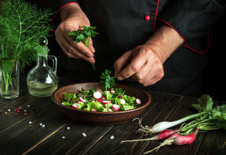 The cook prepares a fresh vegetable salad with his hands in the kitchen. Vegetarian food. hotel menu recipeの写真素材