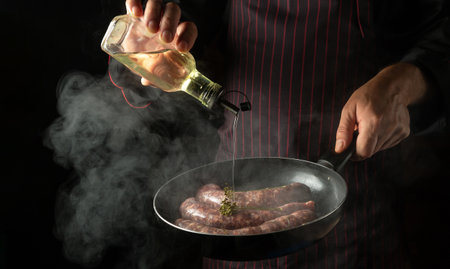 The chef adds oil to a hot frying pan with sausages. Menu or recipe concept for hotel on black background.の写真素材