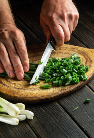 Cook cuts green onion leaves on a vintage cutting board before preparing a delicious dish or a vegetarian dietの写真素材