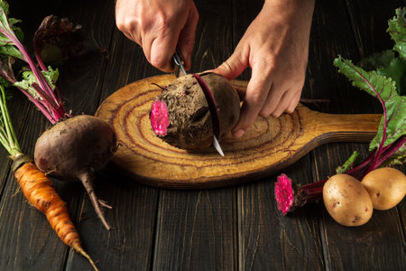 The chef cuts red beets or beetroot on a wooden cutting board. Peasant food.の写真素材