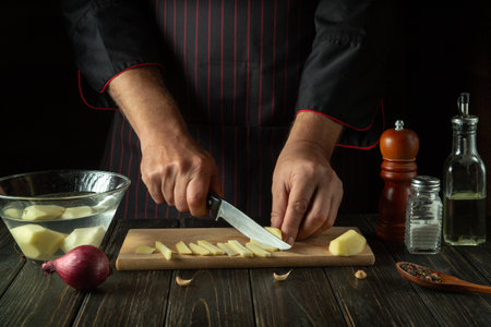 The chef cuts the potatoes into small pieces. Hands of a cook with a knife while preparing delicious food. Vegetable diet menu for restaurant or hotelの写真素材