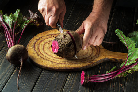 The cook cuts red beets or beetroot on a wooden cutting board. Peasant food.の写真素材