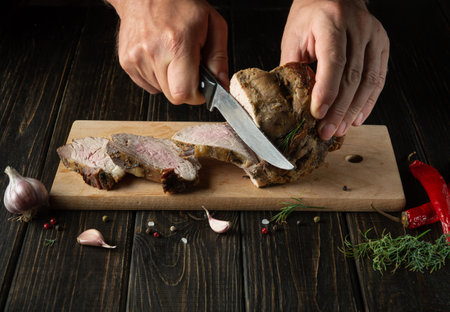 The chef cuts the grilled veal meat into small slices. Work environment on the kitchen table with...