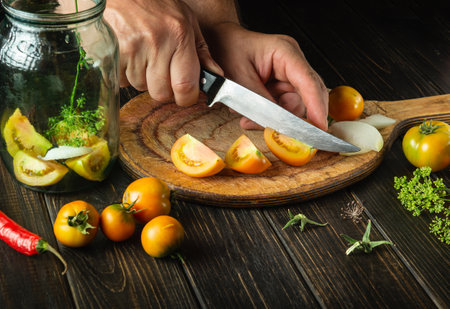 Preparation of canned vegetable salad. Chef hands cut tomatoes on a cutting board with a knife. Peasant food.の写真素材