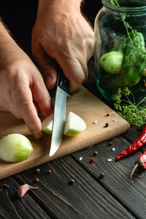 Chef cuts fresh onions for pickling with spices and cucumbers. Close-up of the cook hands while working on the kitchen table. Place for advertisingの写真素材