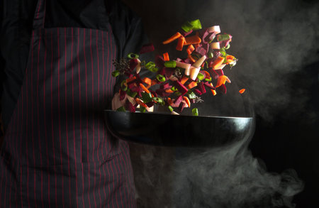 The chef prepares vegetables in a hot pan with steam. The idea of a vegetarian cuisine on a dark backgroundの写真素材