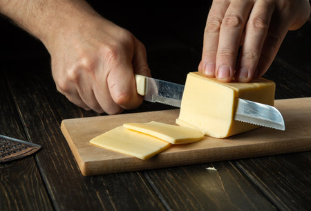 The cook hands with knife cutting a cheese on the wooden board for sandwich, italian pizza or snack in the kitchen. Preparation for cooking. Healthy eating and lifestyle. food conceptの写真素材