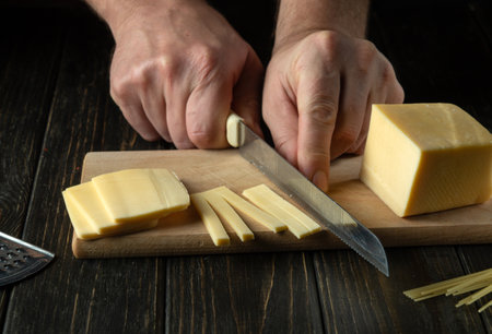 The chef cuts cheese on a cutting board before preparing pizza. Close-up of cook hands with knife on the kitchen tableの写真素材