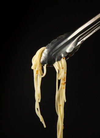 Boiled spaghetti in metal tongs. Delicious food concept with place for recipe or menu on black background.の写真素材