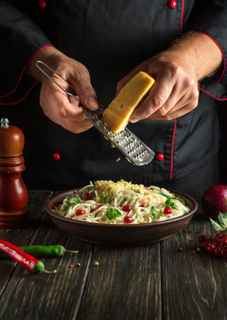 Chef adds hard cheese to spaghetti with spices in a plate. Menu or recipe for a delicious lunch for a hotel or restaurant. copy spaceの写真素材