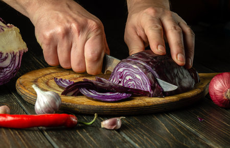 The chef cuts red cabbage with a knife on a kitchen cutting board for salad. Cooking vegetarian food at homeの写真素材