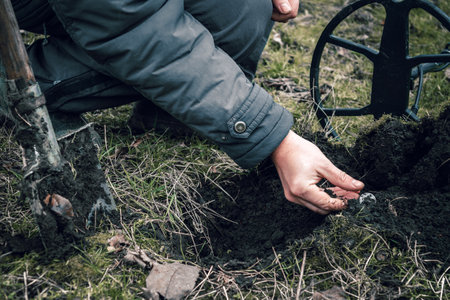 The coin is a lucky find while searching for treasures with a metal detector in the field. The man's hand takes the found ancient coin.の写真素材