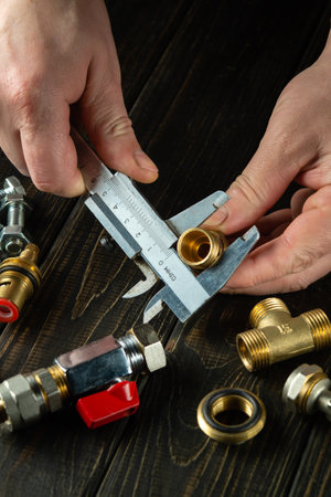 The plumber measures diameter of fitting with a caliper. Working environment in the workshop during...