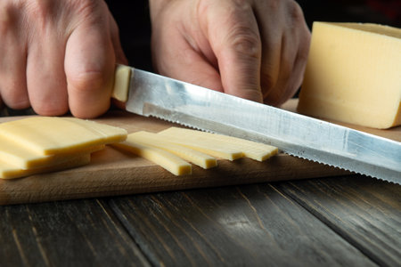 Close-up of a chef hands with a knife slicing cheese on a cutting board in a restaurant kitchen....