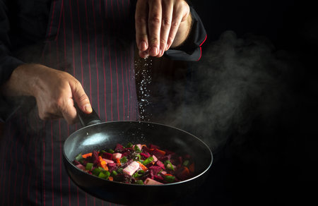 The cook adds salt to a steaming hot pan. Cooking fresh vegetables on the kitchen. copy spaceの写真素材