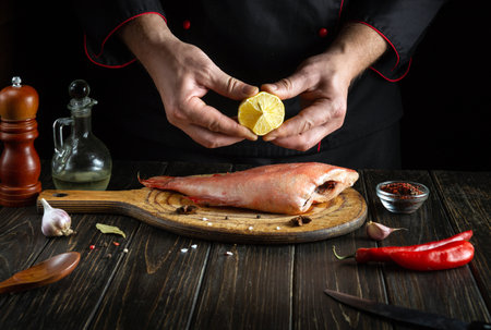 Professional chef presses lemon juice on a Sebastes fish in the kitchen before cooking. The idea of a menu or a delicious recipe for a restaurant on a black backgroundの写真素材