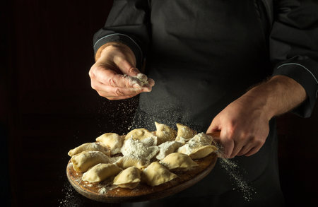 The chef throws flour to raw dumplings on a cutting kitchen board before cooking. Black space for menu or recipe.の写真素材