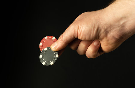 Close-up of a person's hand with two poker chips while betting to win. Free space for advertising on a black backgroundの写真素材