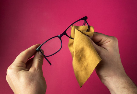 Close-up of a person's hands wiping dust off glasses with a napkin. Reading glasses on red background.の写真素材