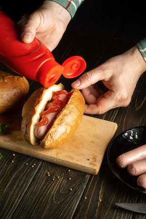 Cooking hot dogs by the hands of a cook on the kitchen table. The concept of cooking fast food or street food.の写真素材