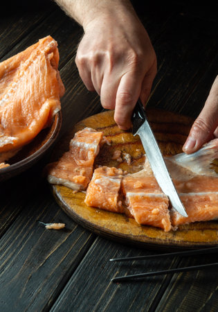 Cutting red fish on a kitchen cutting board before salting. Cook's hands with a knife while cleaning pink salmon. The idea of a fish diet.の写真素材