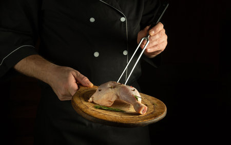 Professional chef prepares lunch with raw chicken leg on the cutting board of the restaurant kitchen. Delicious idea for grilling on black backgroundの写真素材