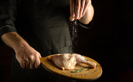 The chef salts the chicken leg before cooking or roasting. Space for recipe or menu on black backgroundの写真素材