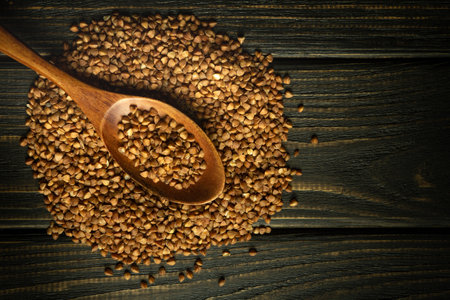 Scattered buckwheat groats on a vintage table and in a wooden spoon. The concept of cooking buckwheat porridge on the kitchen table. Black space for menu or recipe.の写真素材