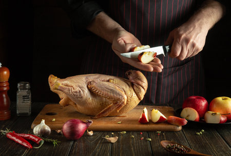 The cook is preparing duck for lunch. Raw duck with apples and spices on the kitchen table. Chef cuts an appleの写真素材