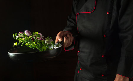 The chef holds a frying pan with flying fresh vegetables. Cooking vegetables for a vegetarian diet in a restaurant kitchen.の写真素材