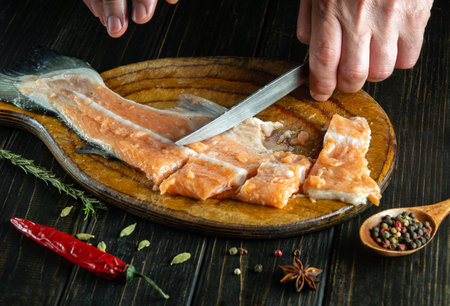 The chef cuts fresh fish with a knife on a wooden cutting board. Delicious fish dish in the kitchen according to an old recipe by the hands of a cook.の写真素材