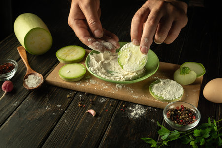 The cook adds flour to the zucchini before roasting with vegetables and an egg. Work environment on the kitchen table with vegetable marrow and spicesの写真素材