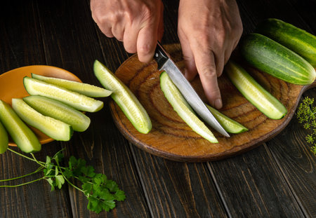 Delicious salad for lunch with fresh cucumber and parsley. Chef hands with knife slicing cucumbers on kitchen cutting board.の写真素材
